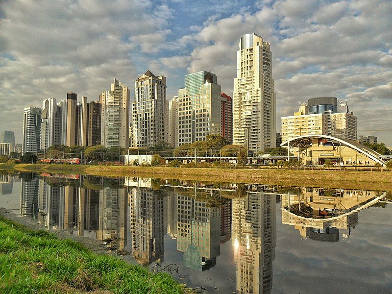 Foto da Marginal Pinheiro, em São Paulo com espelhos d´água. A imagem mostra um bairro cheio de prédios e uma estação de trem, reluzida em um rio.