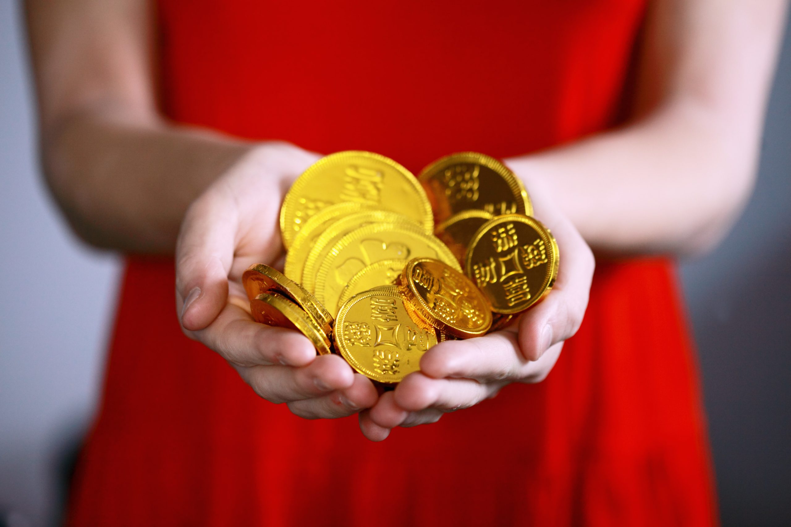 a imagem mostra uma mulher vestida de vermelho segurando moedas douradas representando dinheiro