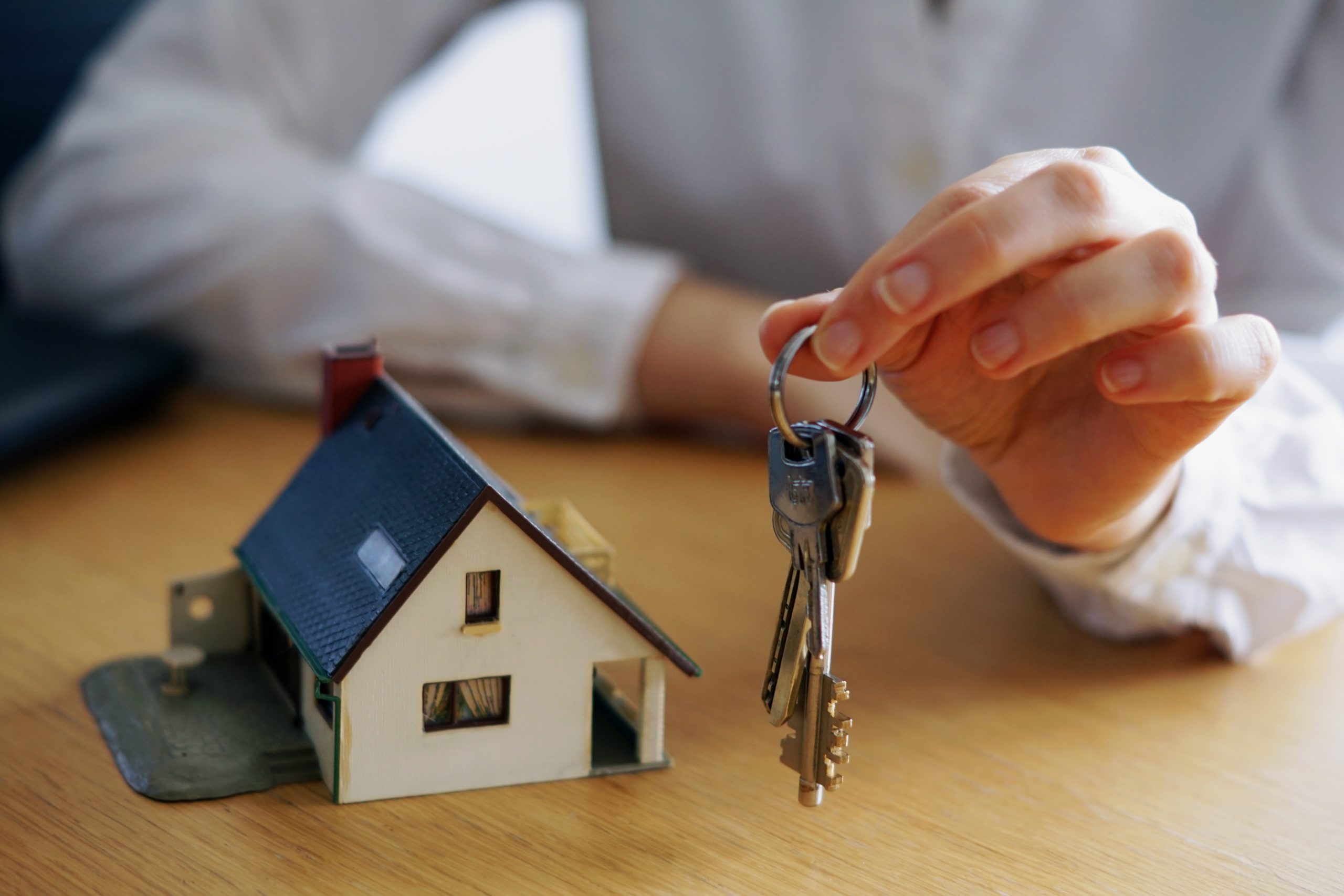 Comprar casa: uma pessoa segura as chaves de um imóvel ao lado de uma miniatura de casa