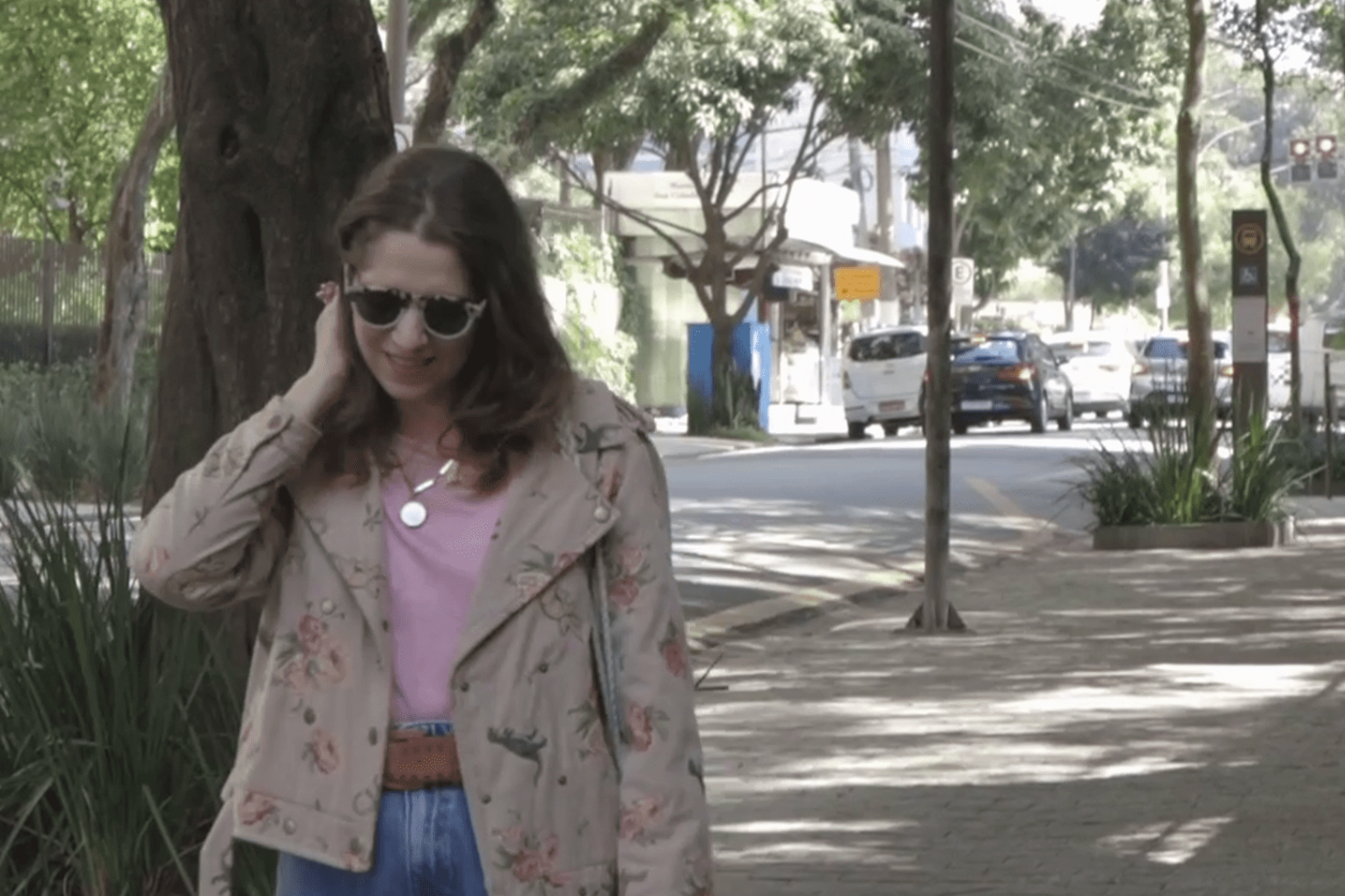 Rolê no bairro: mulher branca de óculos de sol e camiseta rosa andando na calçada de uma rua de Higienópolis.