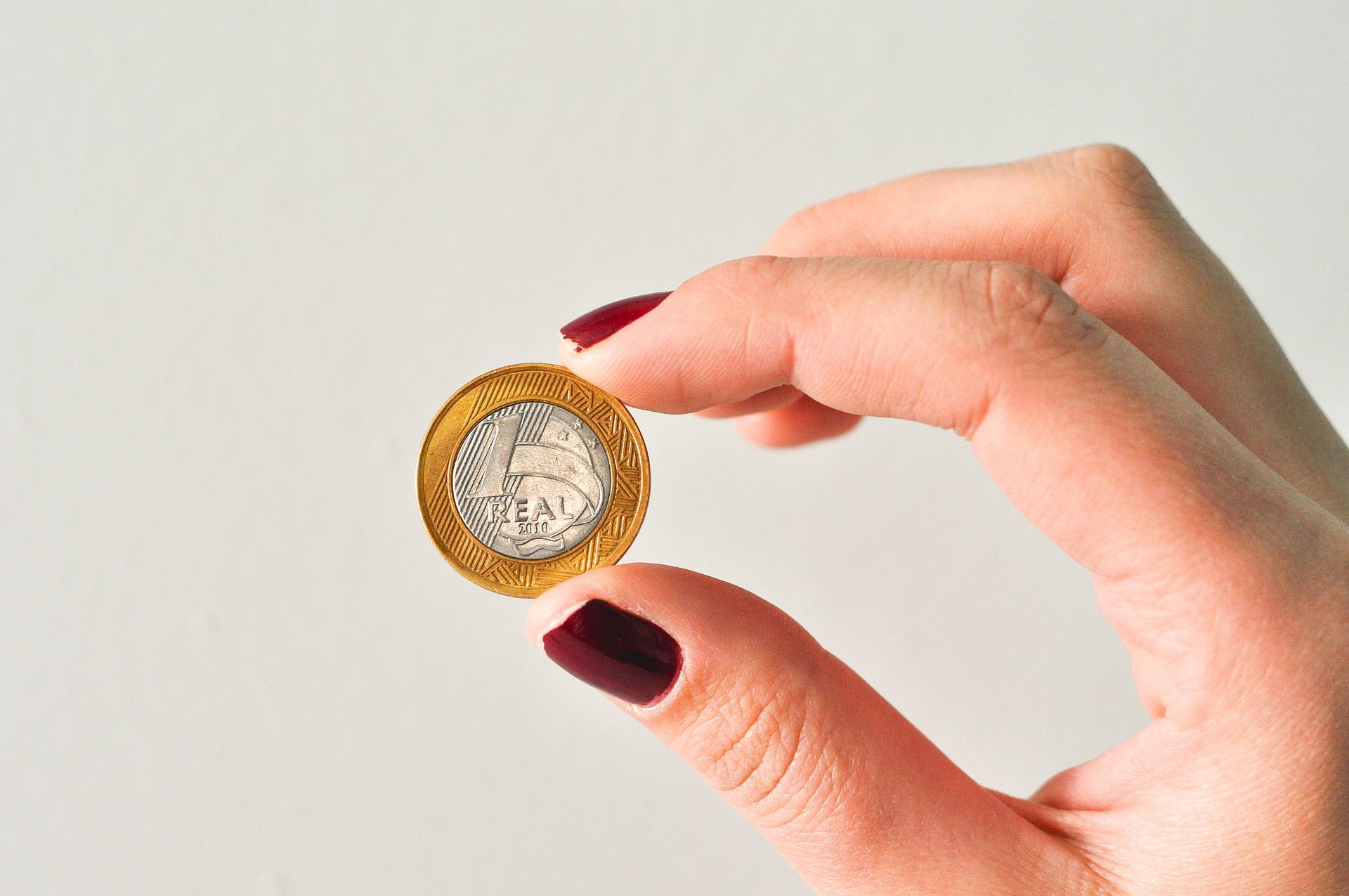 FGTS retido: imagem de uma moeda de um real segurada por uma mão.
