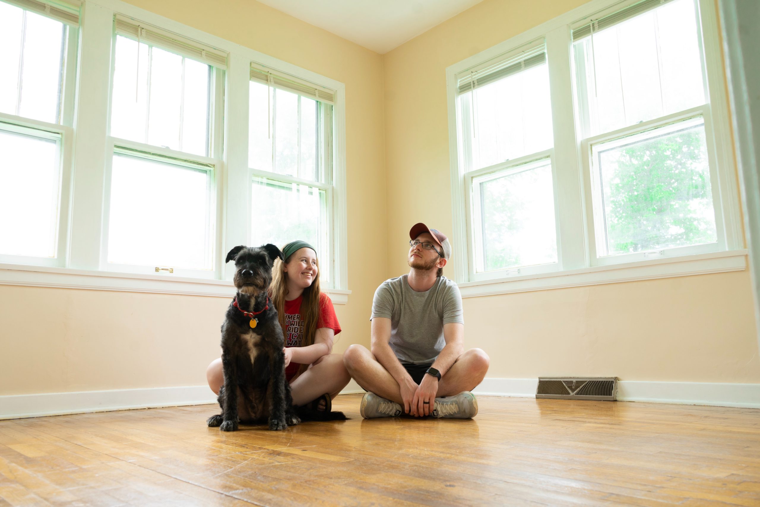 Comprar casa própria: homem, mulher e cachorro sentados no chão de uma casa sem móveis