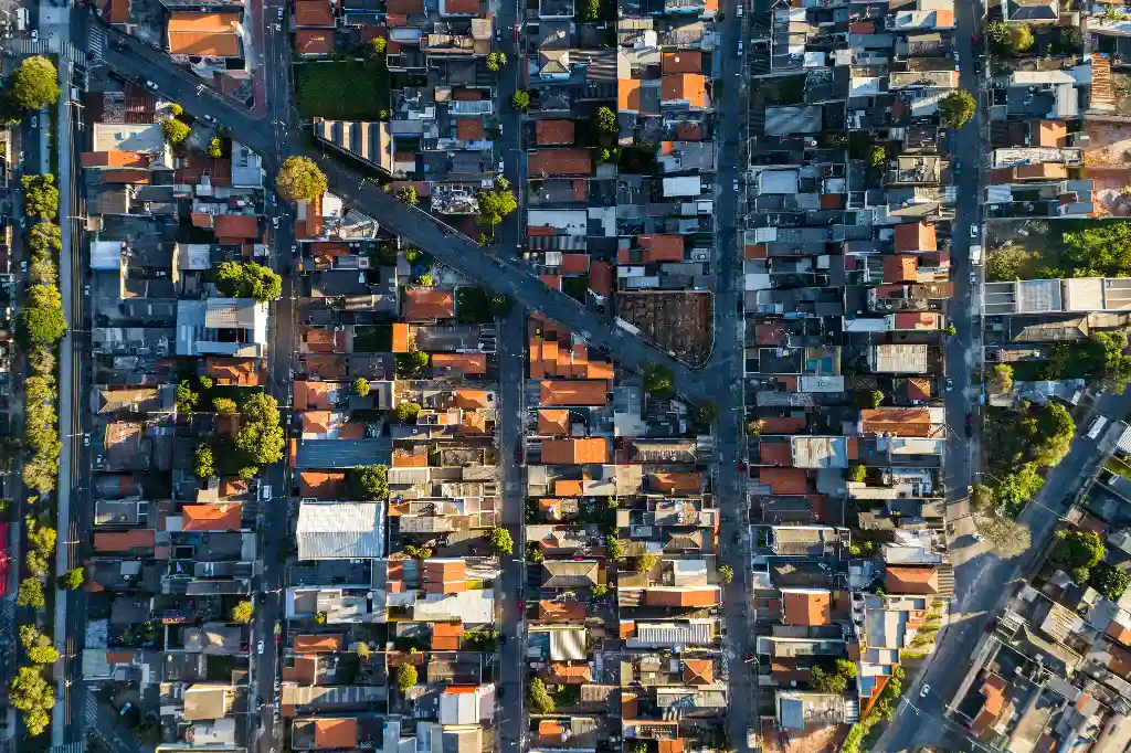 Vista aérea de um bairro residencial com várias casas alinhadas em ruas arborizadas e paisagem urbana.